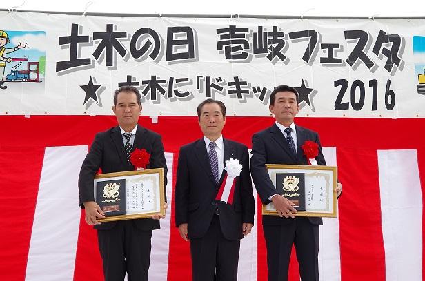 土木の日　壱岐フェスタ2016の横断幕の前で並ぶ白川市長と表彰状を持った2名の男性の写真