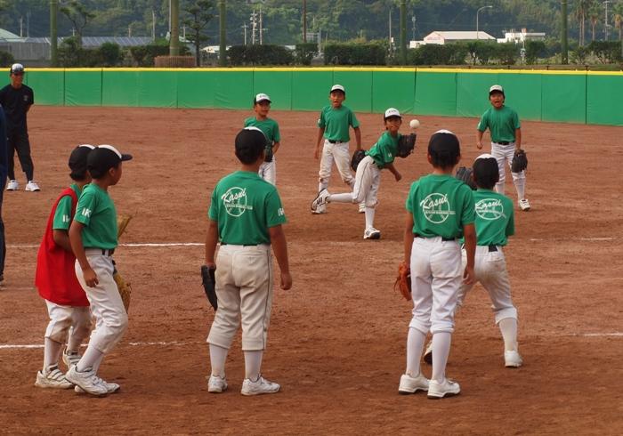 緑色のユニフォームを着たチームの子どもたちがグラウンドでキャッチボールの練習をしている写真