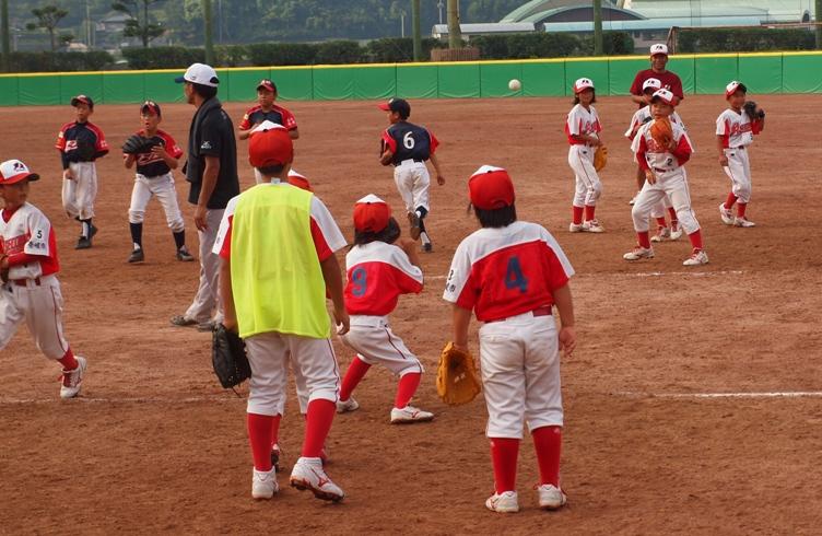 白と赤色のユニフォームを着たチームの子どもたちがグラウンドでキャッチボールの練習をしている写真