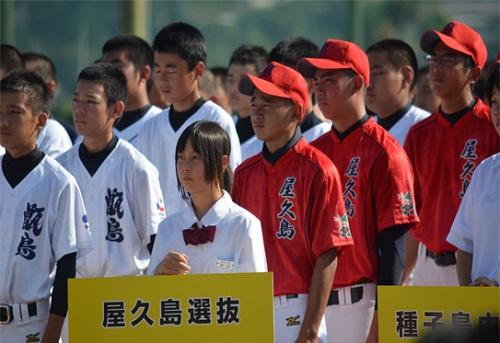 チーム名の書かれたプラカードを持った女子生徒を先頭に赤いユニフォームを着た選手たちが整列している写真