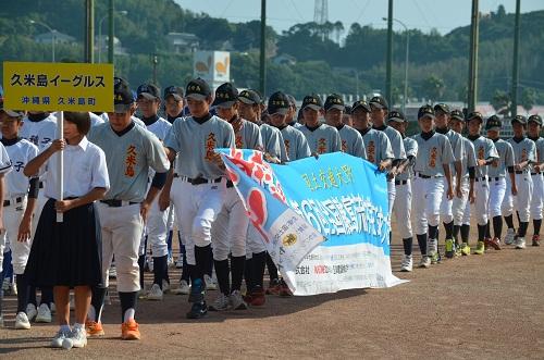 行進している選手が大会名の書かれた横断幕を持っている写真