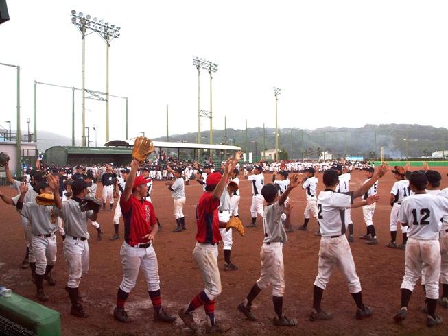 グラウンドで野球のユニフォームを着たたくさんの子ども達が輪になって練習している写真